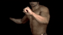 a shirtless man wearing a red bandana and a necklace is dancing in the dark .