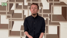 a man in a black shirt stands in front of a wall with the word zin above him