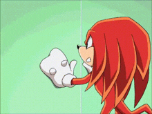 knuckles the echidna from sonic the hedgehog is standing next to a green wall and holding a remote control .