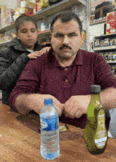 a man sitting at a table with a bottle of water and a bottle of oil