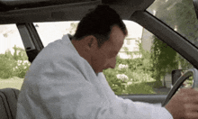 a man in a white coat is sitting in a car looking at his phone .