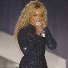 a woman singing into a microphone while wearing a sparkly blue dress