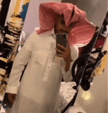 a man is taking a selfie in front of a mirror wearing a head scarf .