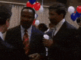 a man in a suit and tie talks to another man in a crowd