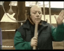a man in a green vest is holding a wooden stick in his hands .