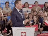 a man in a suit and tie is giving a speech in front of a crowd of people holding flags .