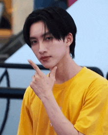 a young man wearing a yellow t-shirt is pointing his finger at his chin .