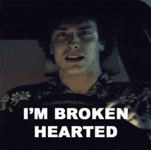 a man sitting in a car with the words i 'm broken hearted