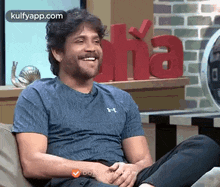 a man is sitting on a couch and smiling while wearing a blue shirt .