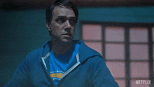 a man in a blue hoodie holds up his hand in front of a netflix sign