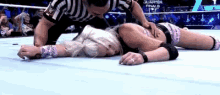a woman is laying on the floor in a wrestling ring with a referee kneeling over her .