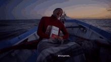 a man sits in a boat holding a book called mbappe