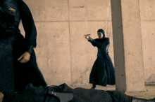 a woman in a black dress is pointing a gun at a man laying on the floor