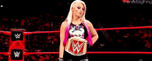 a woman is standing in a wrestling ring holding a wrestling championship belt .