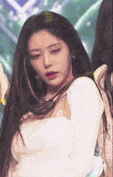 a woman with long hair is wearing a white top and earrings while dancing on a stage .