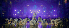a group of dancers are performing on a stage with purple lights behind them
