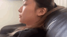 a woman is sitting on a black leather couch with her head resting on the back of the couch .