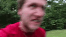 a man in a red shirt is making a funny face in front of trees .