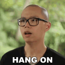 a bald man wearing glasses says hang on in white letters