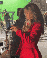 a woman in a red coat is standing in front of a green screen taking a picture of herself