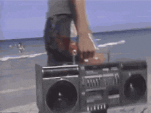 a person is standing next to a boombox on a beach