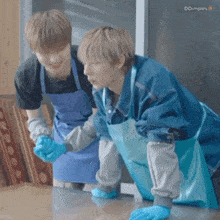 two men in blue aprons are cleaning a table with their hands .