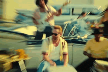 a man is sitting in the back of a car playing a guitar while another man plays drums .