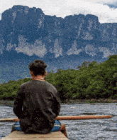 a man sits on a boat looking at a mountain range