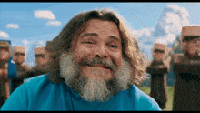 a man with long hair and a beard is smiling in front of a mountain
