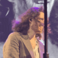 a man with long curly hair is smiling in front of a purple background