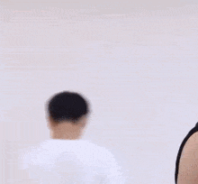a young man in a black tank top is standing in front of a white wall and looking at the camera .