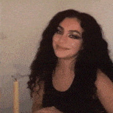 a woman in a black tank top smiles in front of a candle