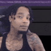 a man with dreadlocks and a tattoo on his arm is sitting in a chair and looking at the camera