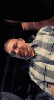 a man wearing glasses and a plaid shirt is looking down