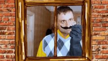 a man with a fake mustache and gloves looks out a window