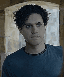 a young man with curly hair is wearing a blue shirt and making a funny face .