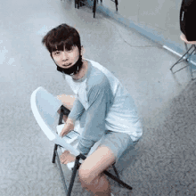 a young man wearing a face mask is sitting on a chair .