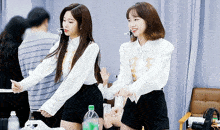 two women are standing next to each other in a room with a bottle of sprite in front of them