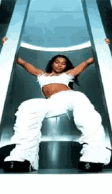 a woman in white pants is standing on a slide with her arms outstretched .