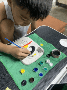 a young boy is painting a picture with a brush on a green towel