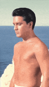 elvis presley without a shirt is standing in front of the ocean