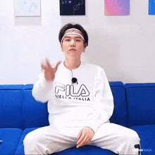 a young man is sitting on a blue couch wearing a white fila sweatshirt .