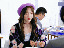 a woman wearing a purple hat is sitting at a table with a plate of food in front of her