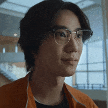 a young man wearing glasses and an orange jacket looks at the camera