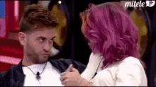 a man with a beard and a woman with pink hair are looking at each other .