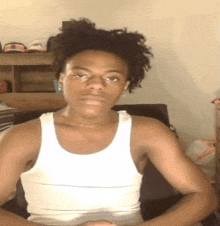 a young man wearing a white tank top is sitting in a chair