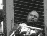 a black and white photo of a man sitting in front of a window playing a violin .