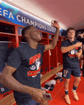 two soccer players celebrate in a locker room with a sign that says champions league