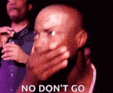 a bald man is covering his mouth with his hand while sitting in a crowd .