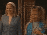 two women are standing next to each other in a room and one of them is holding a bottle of water .